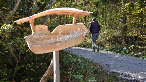 Ein Wegweiser zur Gedenkstätte in einem Wald, ein Mann geht den Weg entlang.