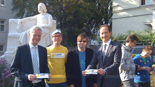 Eine Gruppe von Personen posiert vor einer Statue mit einer Banderole „Licht für die Welt“.