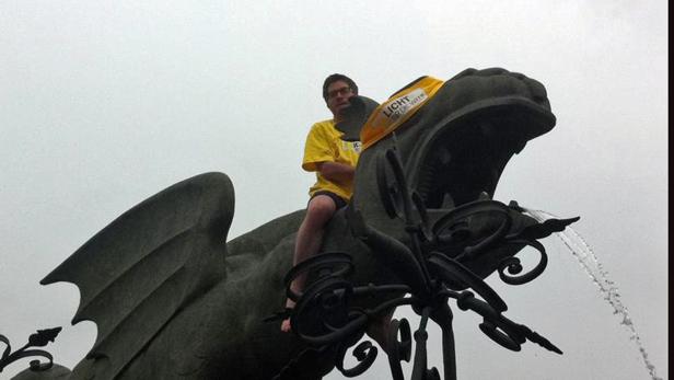 Ein Mann sitzt auf einer Drachenstatue, die Teil eines Brunnens ist.