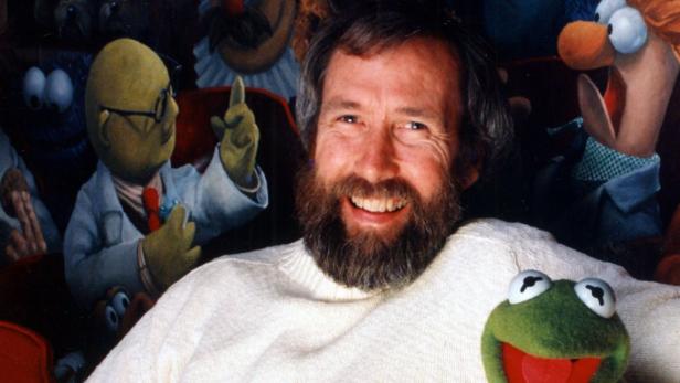 Jim Henson, umgeben von Muppet-Charakteren wie Kermit dem Frosch, lächelt in die Kamera.