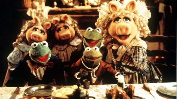 Die Muppets sitzen an einem Tisch mit Speisen, darunter Kermit der Frosch und Miss Piggy.