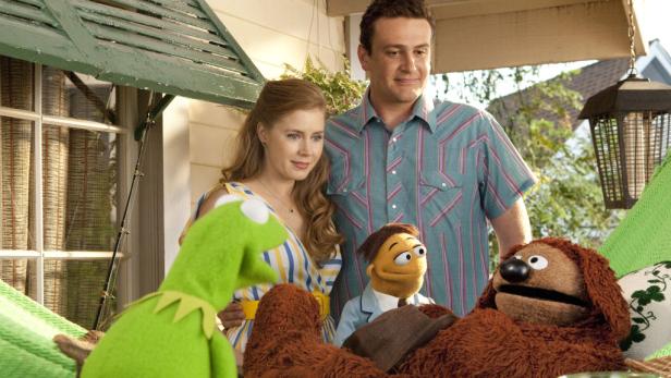 Amy Adams, Jason Segel und mehrere Muppets posieren auf einer Veranda.