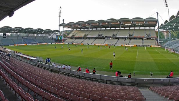 Ein Fußballspiel in einem Stadion mit leeren Sitzen im Vordergrund.