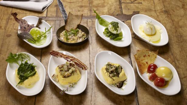Verschiedene Vorspeisen mit Eiern, Gemüse und Speck werden auf einem Holztisch präsentiert.