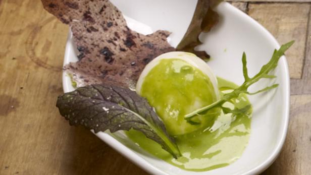 Ein pochiertes Ei mit grüner Sauce, serviert mit Blättern und einer knusprigen Beilage.