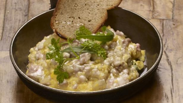 Ein Gericht mit Rührei, Wurst und Brot in einer dunklen Schüssel.