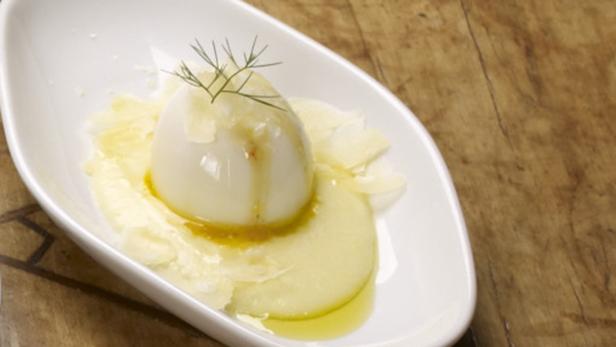 Ein pochiertes Ei mit Apfelscheiben und Dill auf einem weißen Teller.