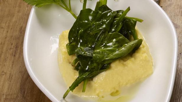 Ein Gericht mit Polenta und Blattspinat auf einem weißen Teller.