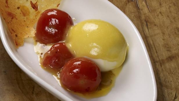 Ein Teller mit Tomaten, einer gelben Kugel und einem knusprigen Chip auf einem Holztisch.