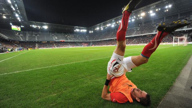 Ein Fußballspieler liegt kopfüber auf dem Rasen in einem Stadion.