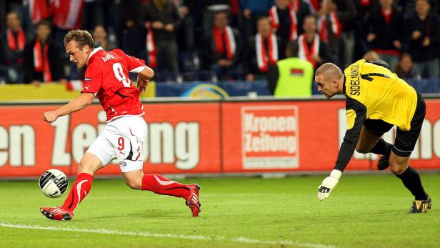 Ein Fußballspieler in Rot schießt den Ball, während ein Torwart in Gelb sich ihm entgegenwirft.