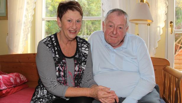 Ein älteres Paar sitzt nebeneinander vor einem Fenster.