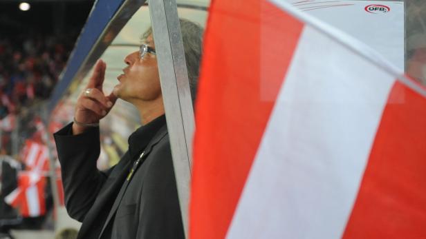 Ein Trainer gibt Anweisungen während eines Fußballspiels, im Vordergrund eine rot-weiße Flagge.