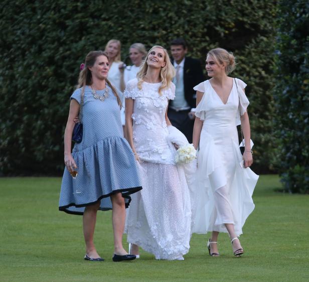 Eine Braut in einem weißen Kleid geht mit zwei Frauen auf einer Wiese entlang.