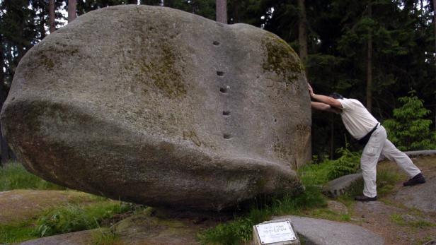 Ein Mann stemmt sich gegen einen großen, ausbalancierten Felsen mit einer Reihe von Löchern.