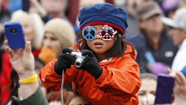 Ein Mädchen mit Friedenszeichen-Sonnenbrille sitzt auf den Schultern einer Person und fotografiert.