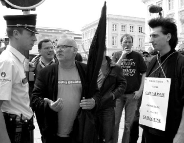Ein Mann mit Brille gestikuliert während einer Demonstration mit einem Polizisten.