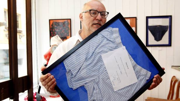 Ein Mann präsentiert ein gerahmtes, gestreiftes Herrenhemd mit einer Notiz in einem Museum.