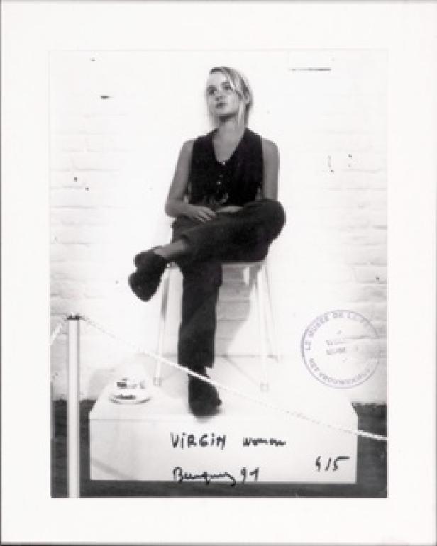 Eine junge Frau sitzt auf einem Hocker vor einer weißen Ziegelwand.