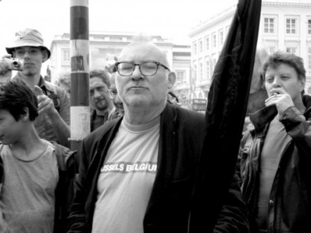 Ein Mann mit Brille und T-Shirt mit der Aufschrift „Brussels Belgium“ steht in einer Menschenmenge.