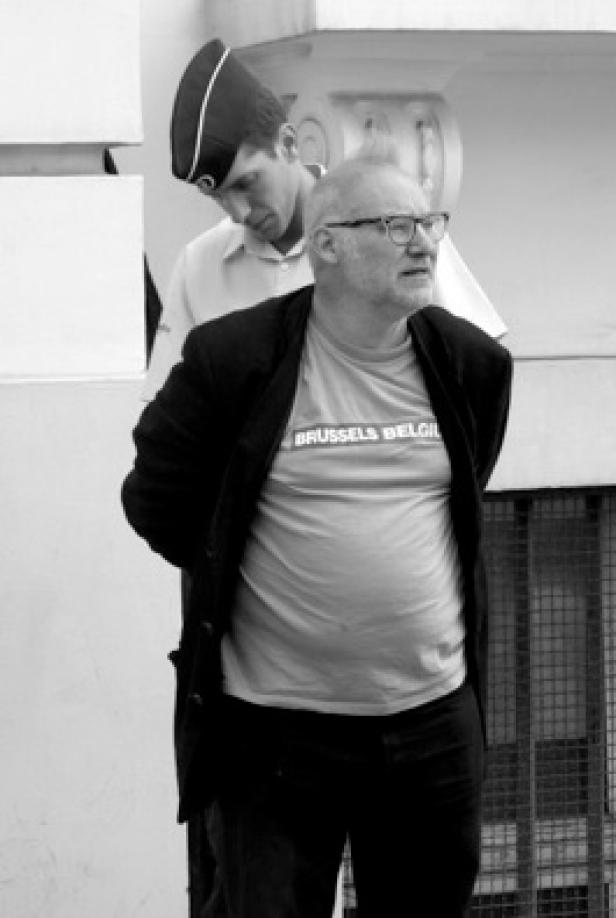 Ein Mann mit einem T-Shirt mit der Aufschrift „Brussels Belgium“ wird von einem Polizisten abgeführt.