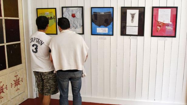 Zwei Männer betrachten eine Kunstausstellung mit gerahmten Unterhosen an einer weißen Wand.