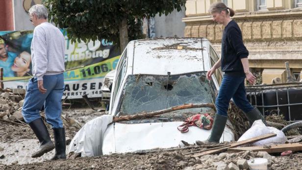 Zwei Personen gehen an einem durch eine Überschwemmung beschädigten Auto vorbei.