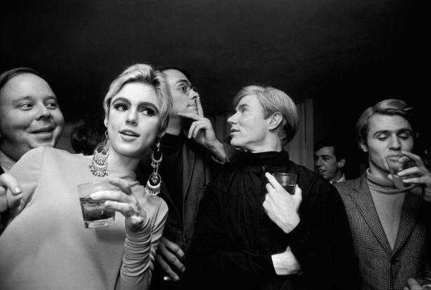 Schwarzweißfoto einer Party mit Andy Warhol und anderen Gästen, die Getränke halten.