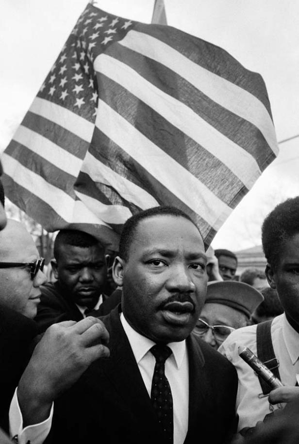 Martin Luther King Jr. spricht vor einer US-Flagge zu Reportern.