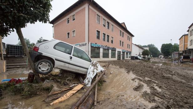 Ein weißes Auto ist bei einer Überschwemmung gegen einen Baum gespült worden.