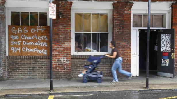 Eine Frau schiebt einen Kinderwagen vor einem Gebäude mit verbarrikadiertem Fenster entlang.
