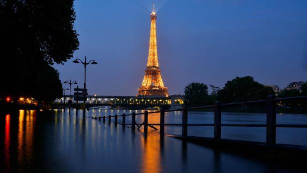 Der Eiffelturm erstrahlt nachts über der Seine in Paris.
