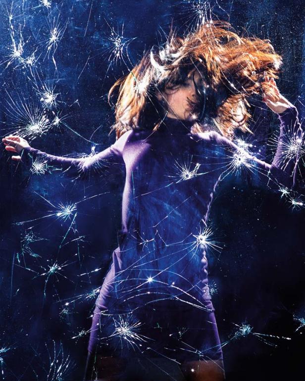 Eine Frau in einem lila Kleid posiert vor einer zerbrochenen Glasscheibe.