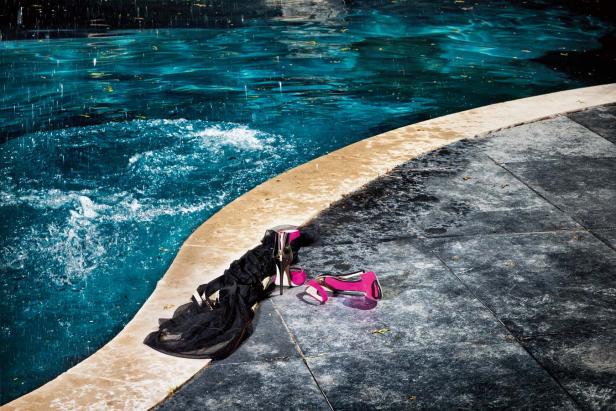 Ein Paar pinke High Heels und ein schwarzes Kleid liegen am Rand eines Pools.