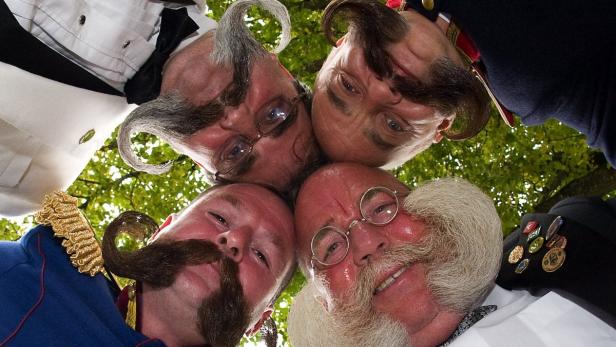 Vier Männer mit extravaganten Bärten und Schnurrbärten blicken in die Kamera.