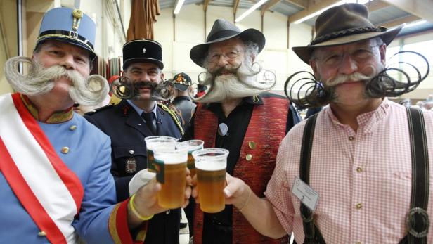 Männer mit kunstvoll gezwirbelten Bärten stoßen mit Bier an.