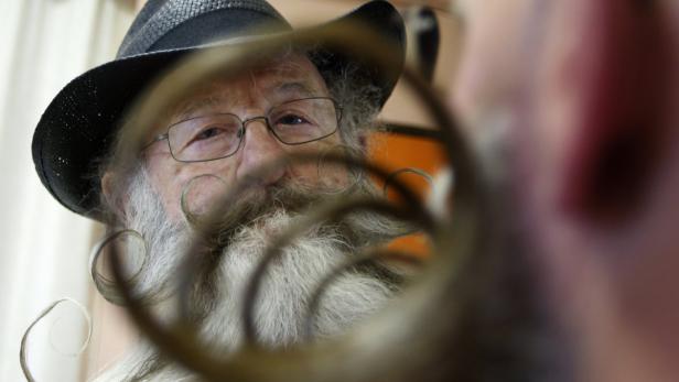 Ein älterer Mann mit Hut, Brille und einem langen, gezwirbelten Bart.