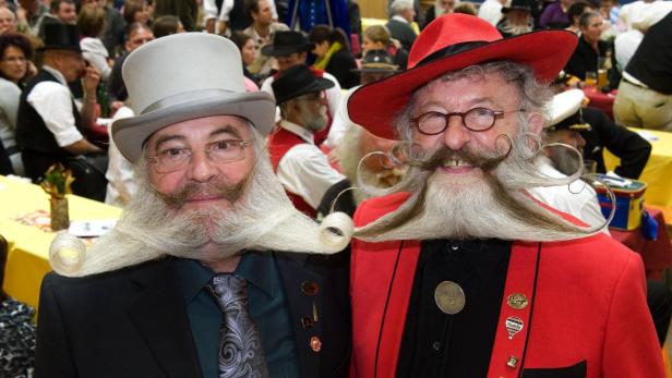 Zwei Männer mit extravaganten Bärten und Hüten posieren für ein Foto.