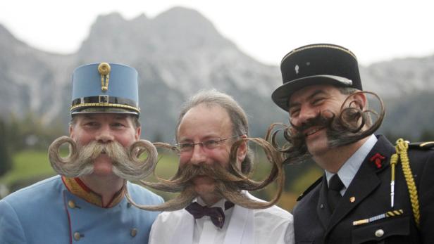 Drei Männer mit extravaganten Bärten und Uniformen posieren vor einer Bergkulisse.