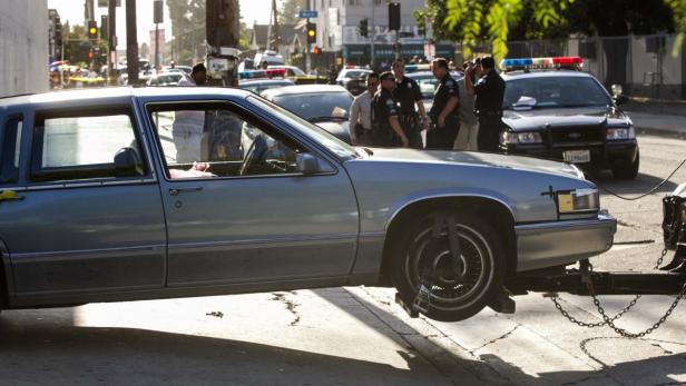 Ein abgeschlepptes Auto steht auf einer Straße, während Polizisten im Hintergrund stehen.