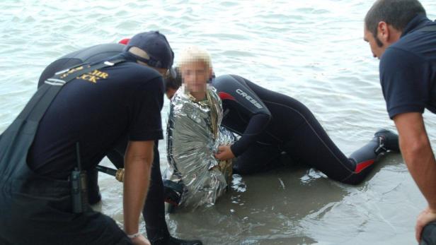 Ein Kind wird am Ufer von Rettungskräften in eine Rettungsdecke gehüllt.