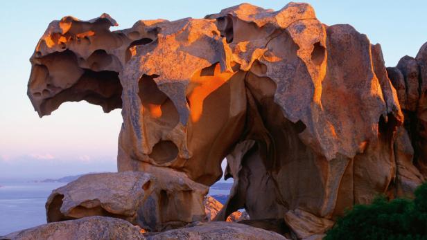 Ein großer, zerklüfteter Felsen mit Löchern steht an der Küste.