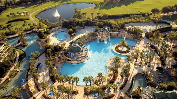 Ein Resort mit mehreren Pools, Palmen und einem Golfplatz im Hintergrund.