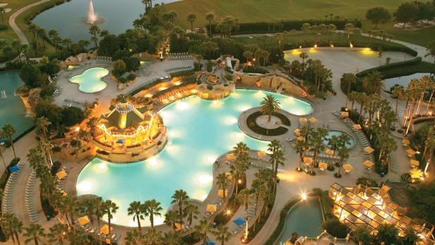 Ein Resort mit mehreren Pools, Palmen und einem See bei Dämmerung.