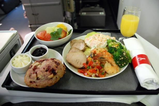 Ein Tablett mit einer Mahlzeit, bestehend aus Fleisch, Salat, Obst und einem Getränk, im Flugzeug.