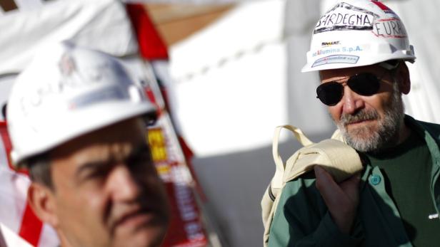 Zwei Männer, einer mit Sonnenbrille und Bauhelm mit der Aufschrift „Sardegna“.