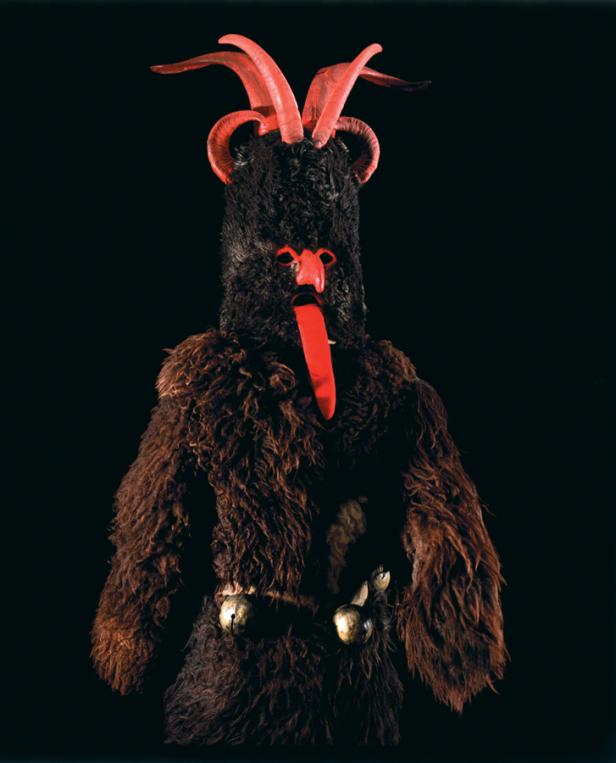 Eine traditionelle Krampus-Maske mit roten Hörnern und einer langen Zunge vor schwarzem Hintergrund.