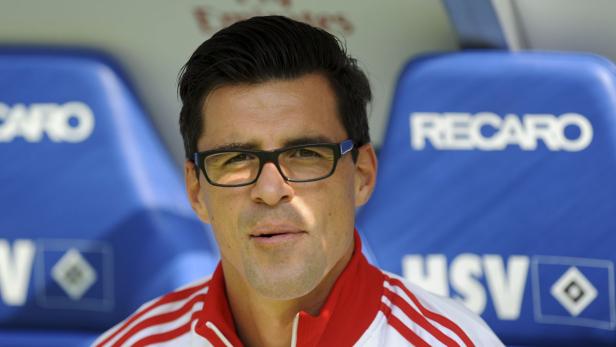 Ein Mann mit Brille und rot-weiß gestreifter Jacke sitzt auf einer blauen Bank mit der Aufschrift „RECARO“.