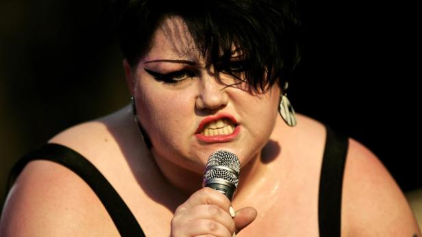 Eine Sängerin mit schwarzem Haar singt mit einem Mikrofon in der Hand.