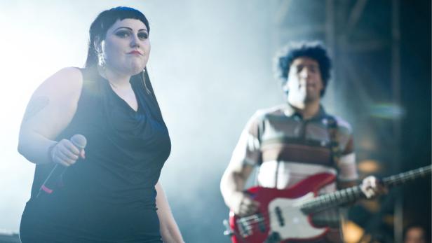 Eine Sängerin mit Mikrofon und ein Gitarrist treten auf einer Bühne auf.